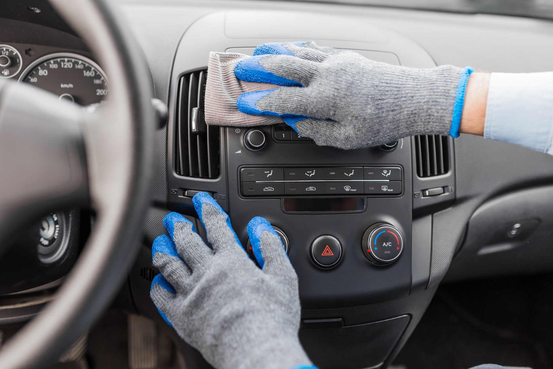 Car wash worker maintaining and detailing car interior console shine by using microfiber cloth. Car detailing or valeting concept.